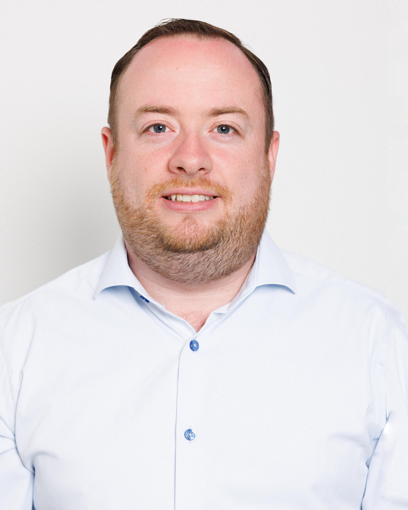 Head-and-shoulders portrait of a smiling man in a light blue button-down shirt against a plain white background, suitable as a professional headshot.