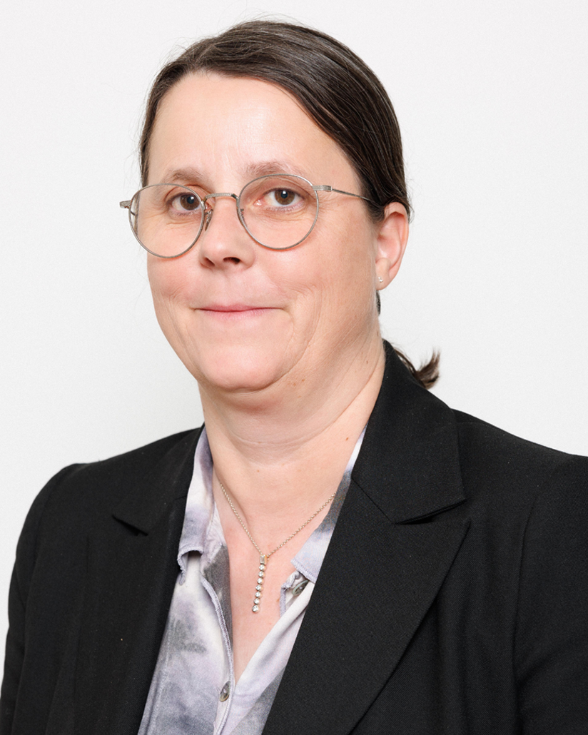 Head-and-shoulders portrait of a woman with round glasses, wearing a black blazer and a light-gray blouse.